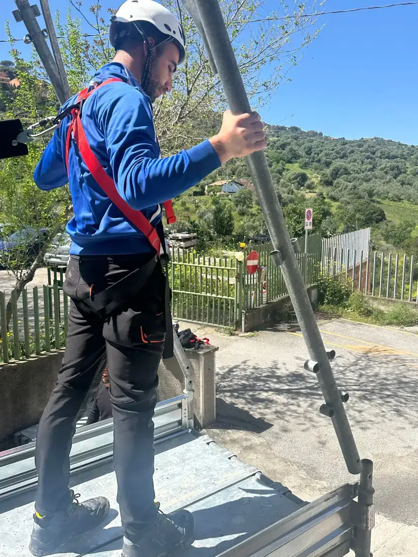 Un partecipante sale su un ponteggio con casco e imbracatura durante l’esercitazione pratica